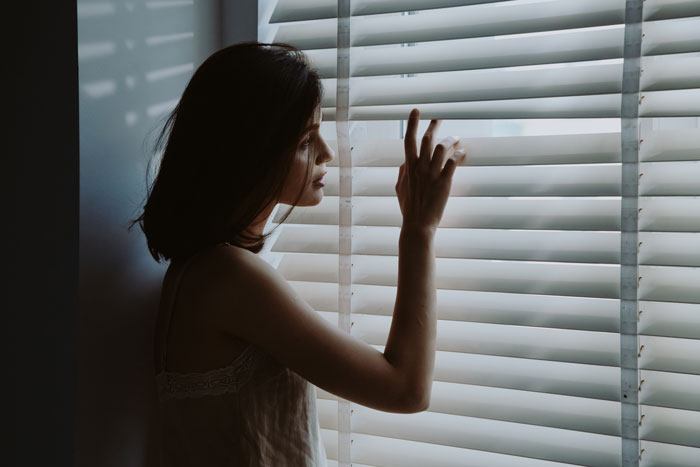 mujer con las persinas cerradas mirando ventana trucos para casa fresca sin aire