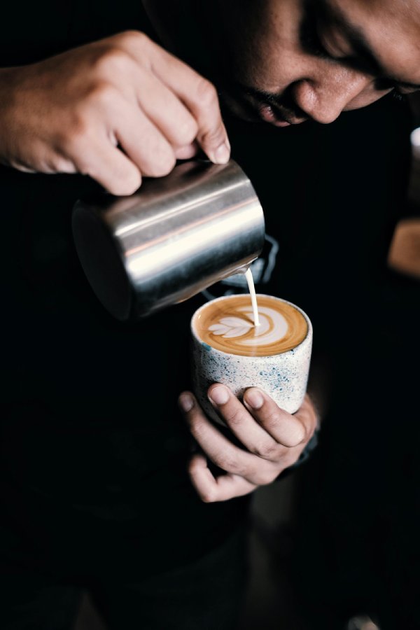 barista hombre sirviendo leche sobre café espuma