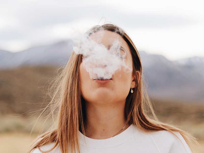 Chica fumando y echando humo.