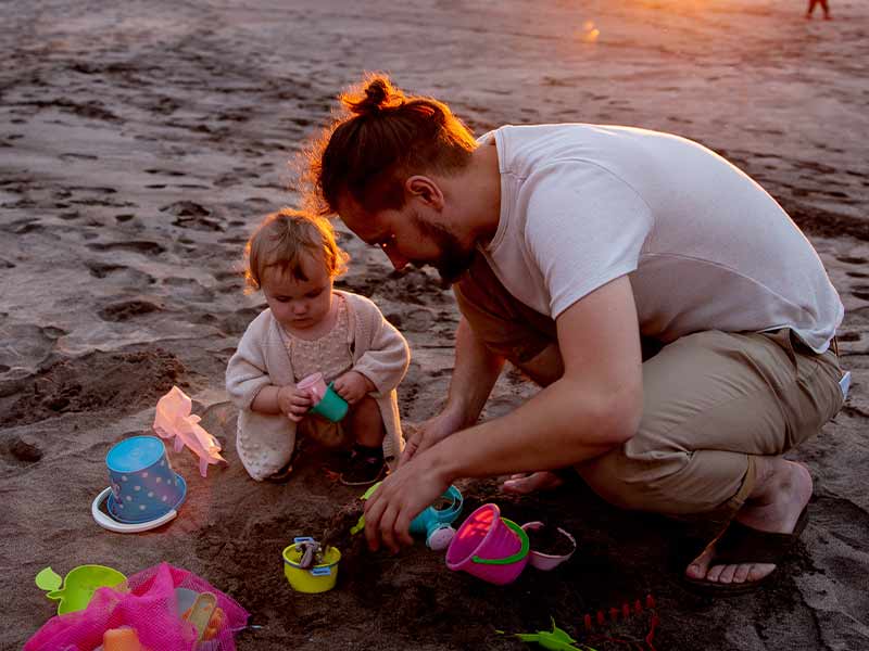 Un padre jugando con su hija en la arena de la playa.