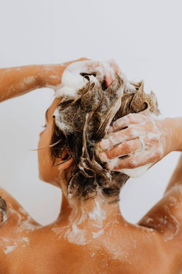 mujer lavandose la cabeza con jabón masajeando