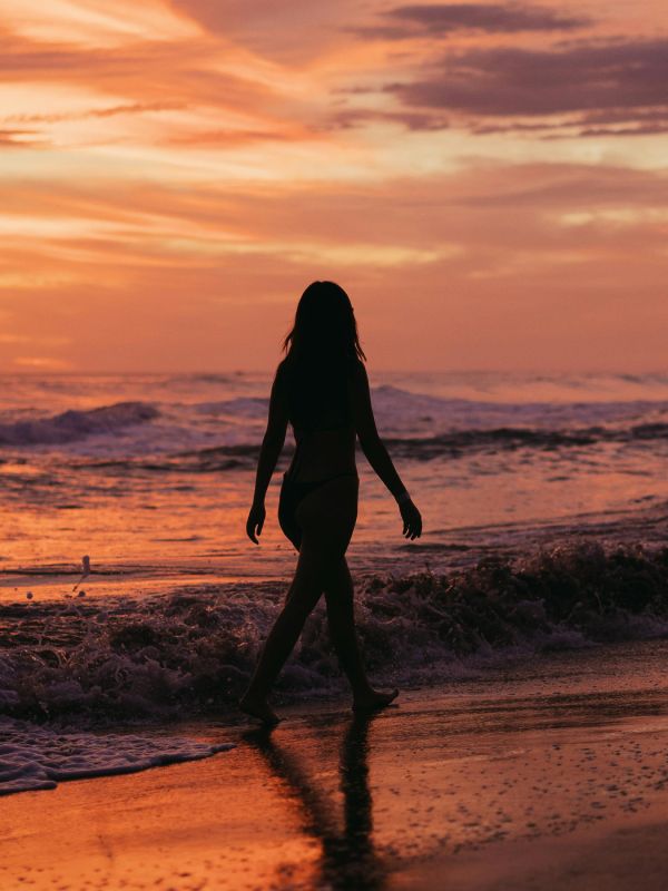 Mujer paseando por la playa al anochecer